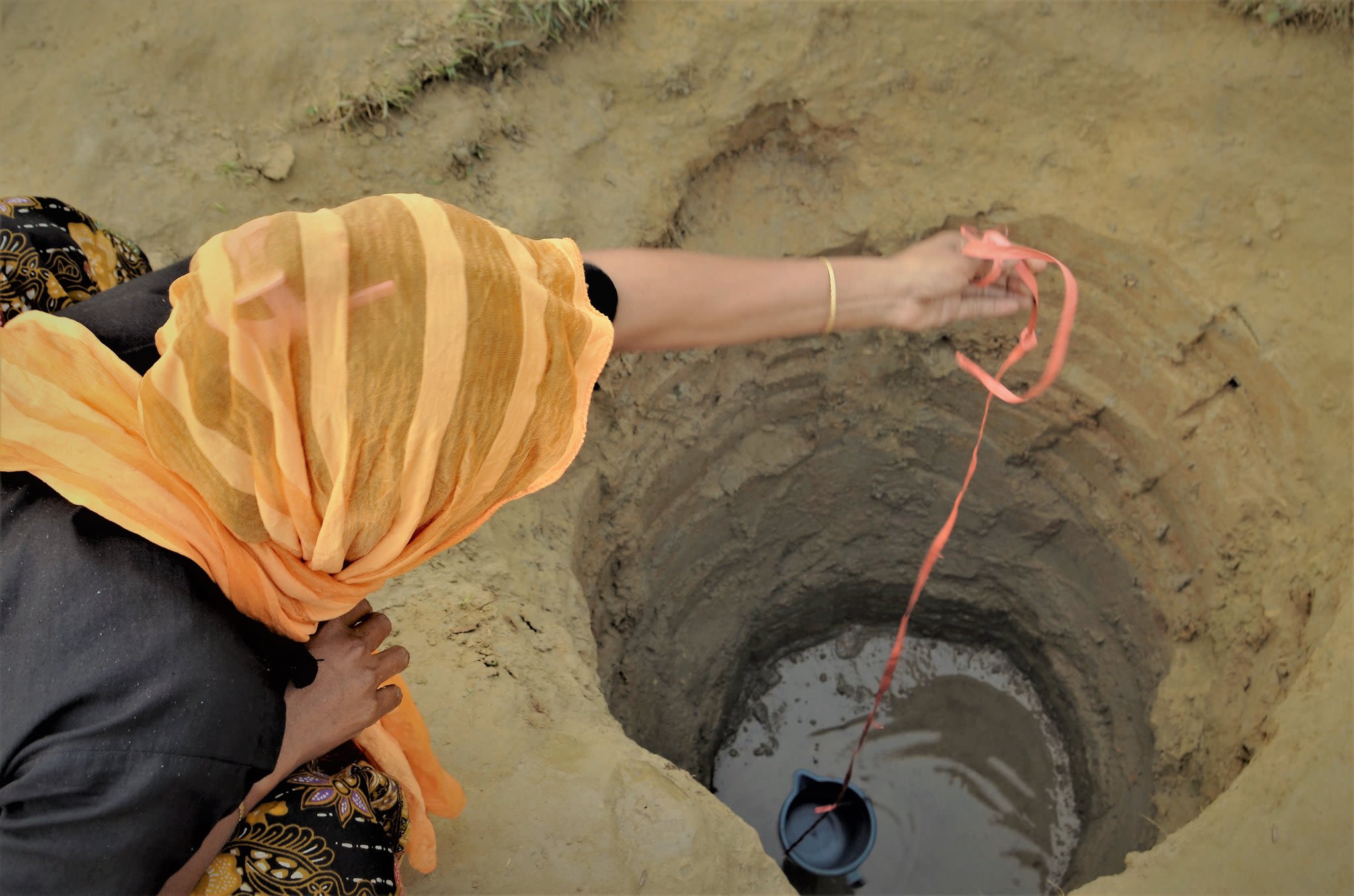 Image of woman drawing water from water hole by Abul Kalam